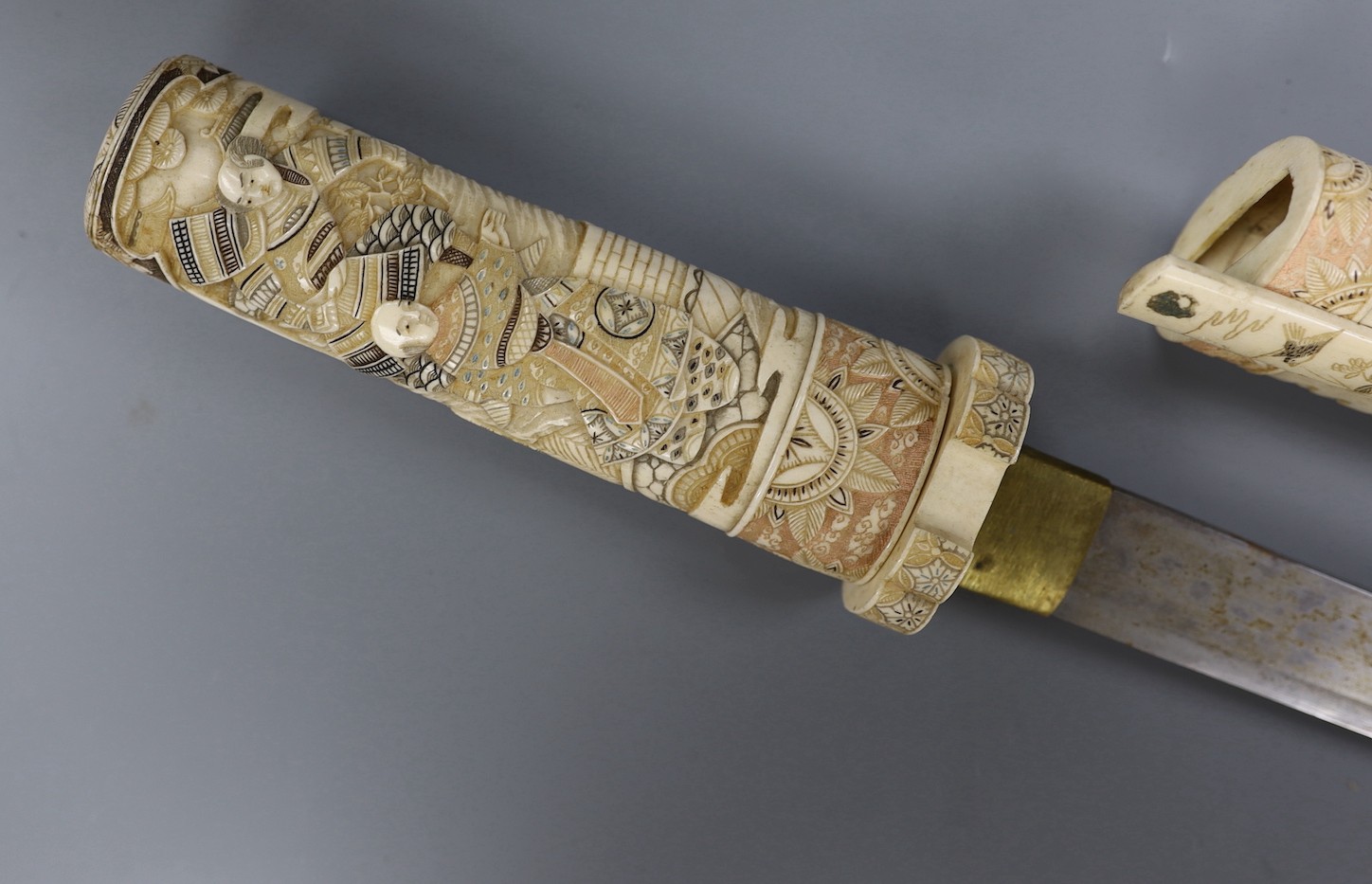 A Japanese carved and coloured ivory tanto, Meiji period, the hilt and scabbard carved to both sides with figures in ceremonial dress, the whole etched in black , green and red, the separate kodzuka with ivory blade and